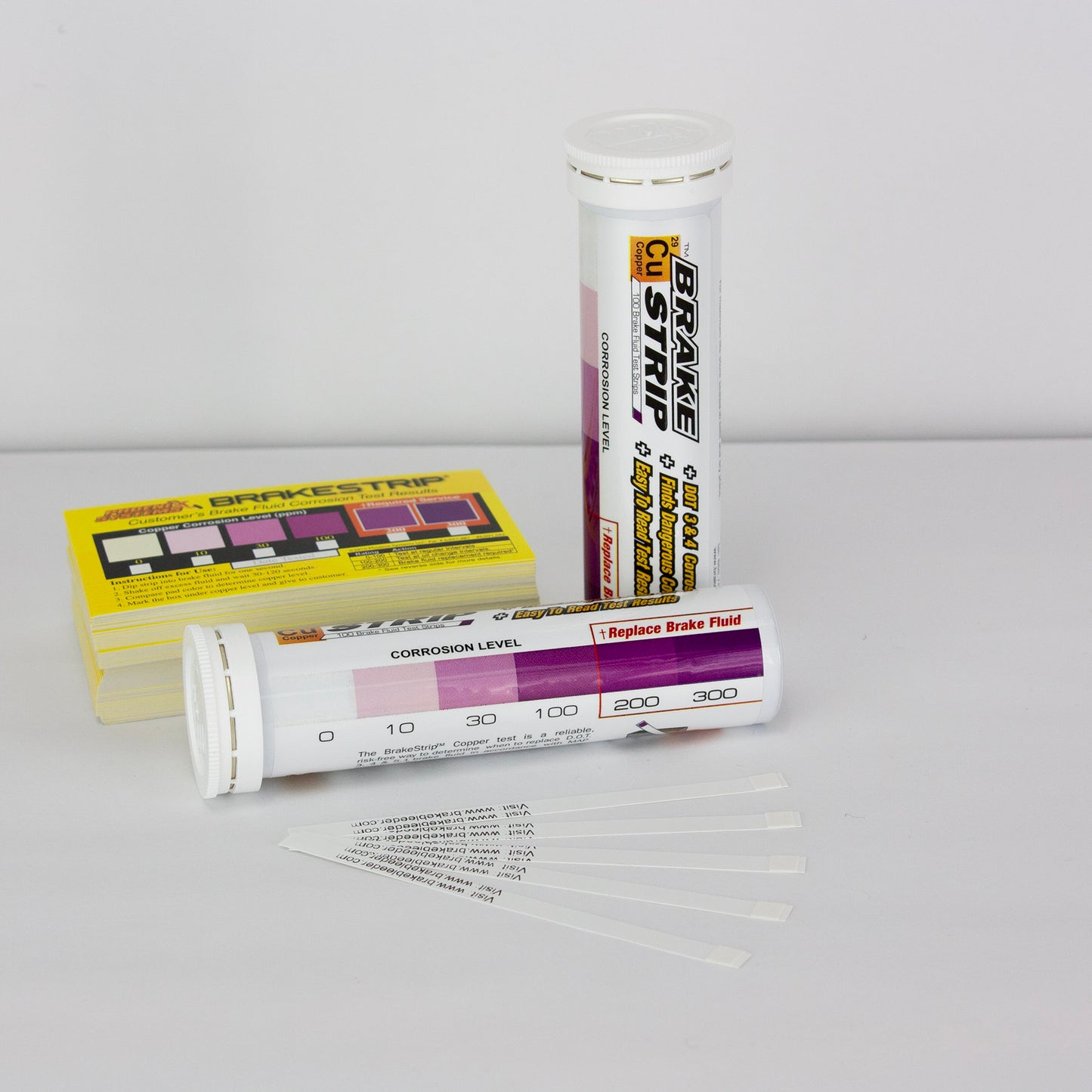 The image shows two containers of Phoenix Systems Brake Fluid Test Strips. One container is a tube and the other is a box. Text on the containers describes the product and its function. There is also a chart that appears to indicate a range of corrosion levels.