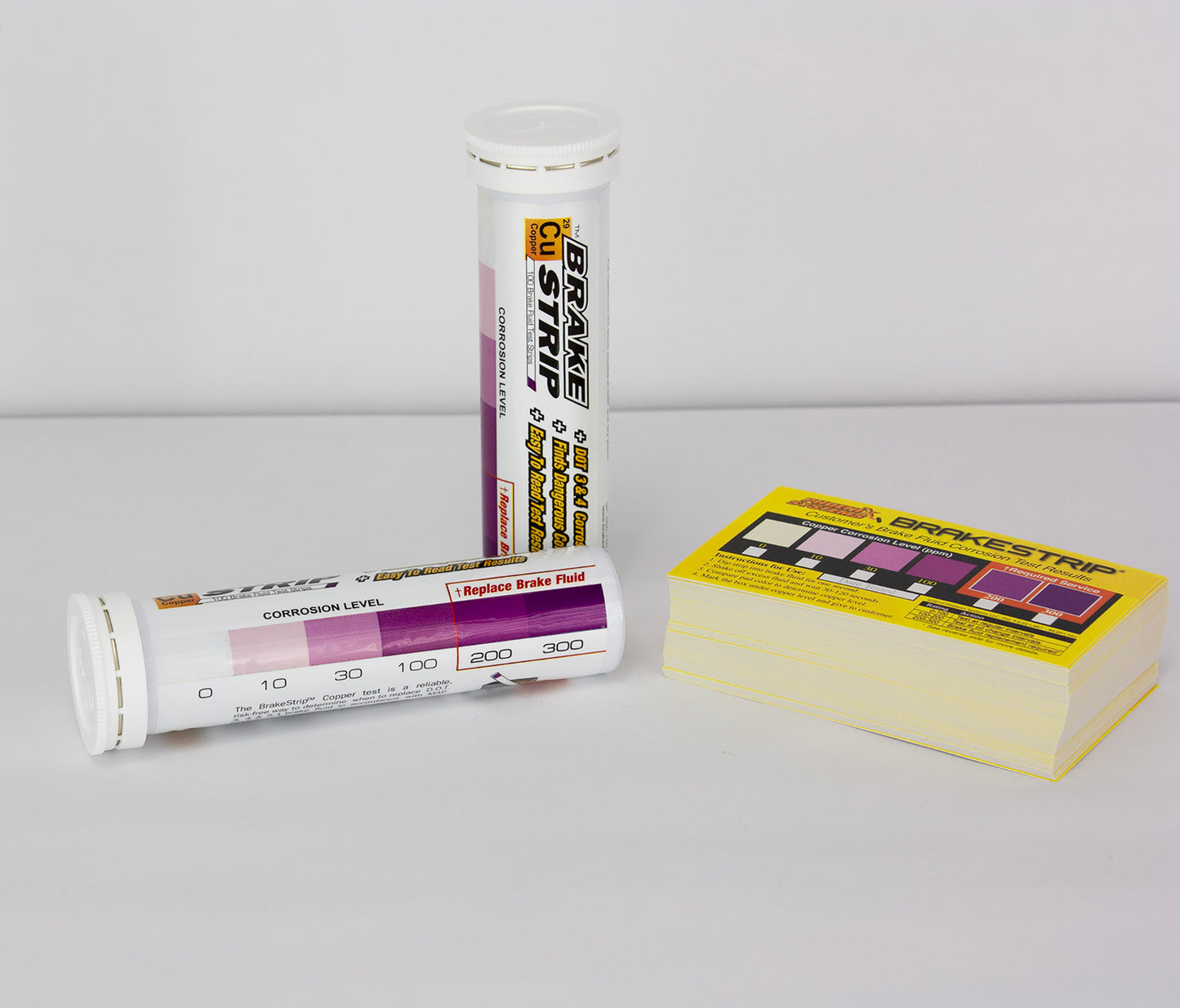 The image shows two containers of Phoenix Systems Brake Fluid Test Strips. One container is a tube and the other is a box. Text on the containers describes the product and its function. There is also a chart that appears to indicate a range of corrosion levels.