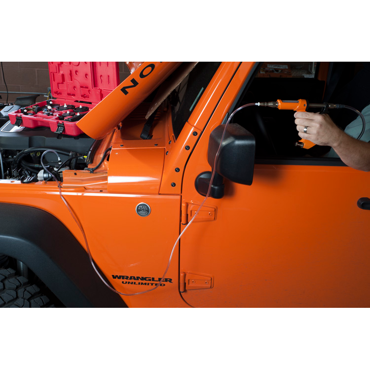 The image shows a man using a tool to bleed the brake fluid of an orange Jeep Wrangler. The brake fluid bleeding gun is connected to a hose that is attached to the brake caliper of the Jeep