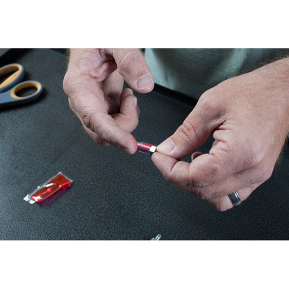 The image is a close-up of a man’s hands holding a small, round object with a hole in the center. The object is most likely a brake fluid bleeder screw cap and putting red grease on it