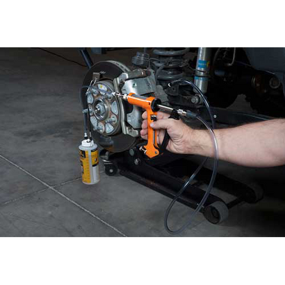 The image shows a mechanic using a brake fluid bleeding gun to bleed a brake caliper on a car.