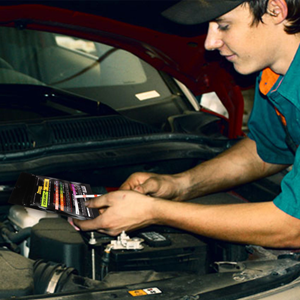 The image depicts a person holding a package of coolant and brake fluid test strips in front of a car engine