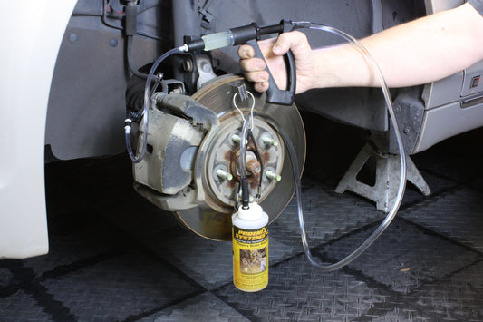 The image shows a mechanic using a brake fluid bleeding gun to bleed a brake caliper on a car.