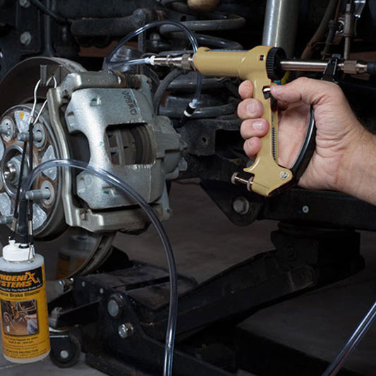 The image shows a mechanic using a brake fluid bleeding gun to bleed a brake caliper on a car.